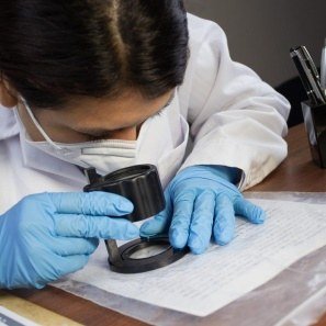 A gloved hand examining a document with a magnifying loupe
